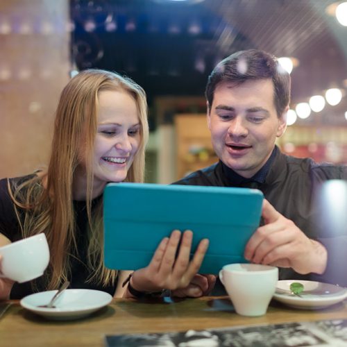 Happy young man and woman drinking coffee while looking on tablet